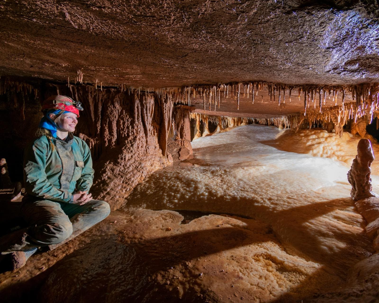 A Hypogenica researcher exploring a cave passage lined with carbonate formations.